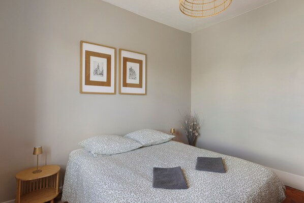 A bedroom with a bed, a nightstand, a lamp, and two framed pictures on the wall.