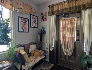 A cozy living room with a sofa, decorative pillows, wall art, and a door with curtains. - 146-2 Satchmo, Louie Armstrong. Chocolatey Jazz Lounge w/Mini Rolling Desk. (New London)