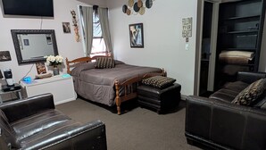 A bedroom with a bed, two leather sofas, a desk with a coffee maker, a mirror, and a wardrobe. - 146-2 Satchmo, Louie Armstrong. Chocolatey Jazz Lounge w/Mini Rolling Desk. (New London)