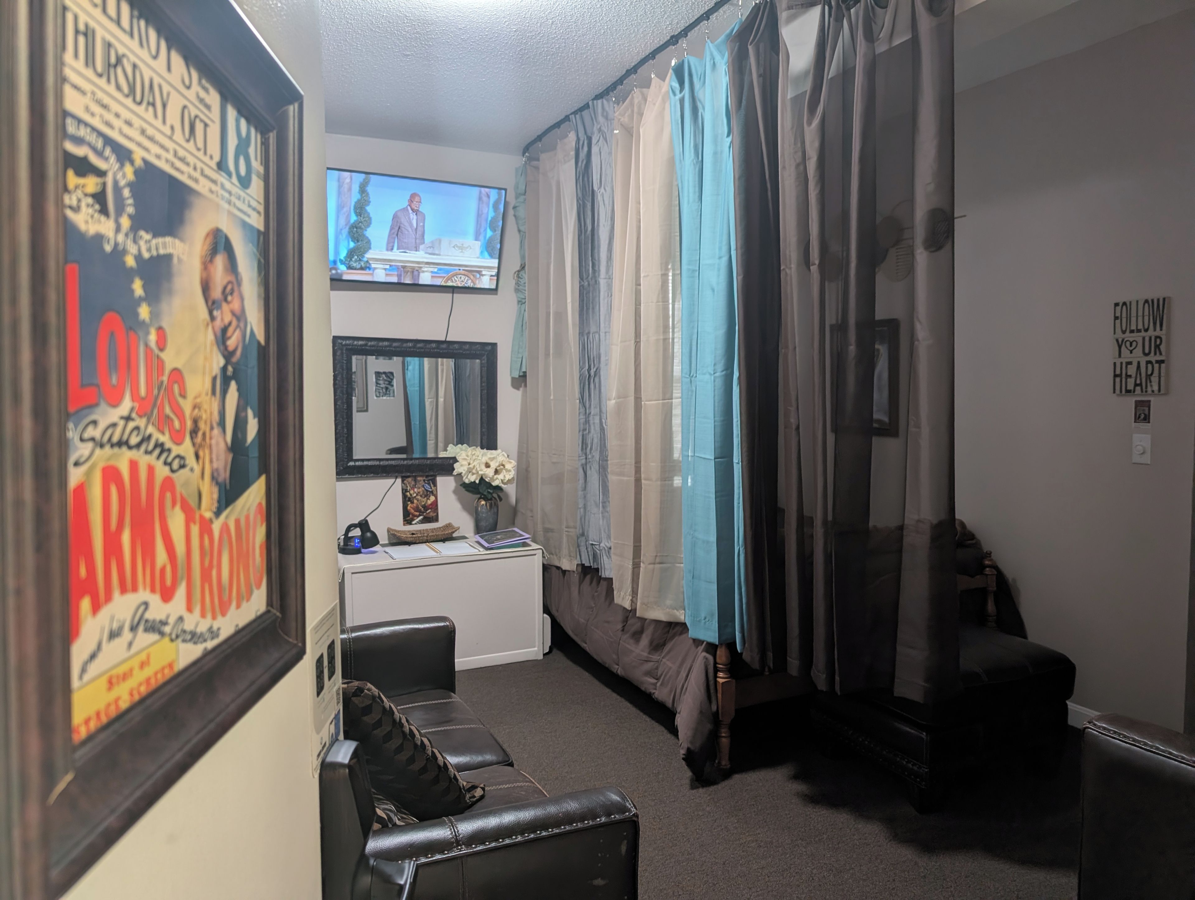 A room with a television, a framed poster, a desk with a vase of flowers, a couch, and a chair.
