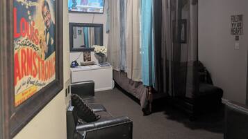 A room with a television, a framed poster, a desk with a vase of flowers, a couch, and a chair.
