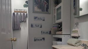 A bathroom with a toilet, sink, and wooden cabinets. There are towels hanging on the wall and a trash can. - 146-2 Satchmo, Louie Armstrong. Chocolatey Jazz Lounge w/Mini Rolling Desk. (New London)