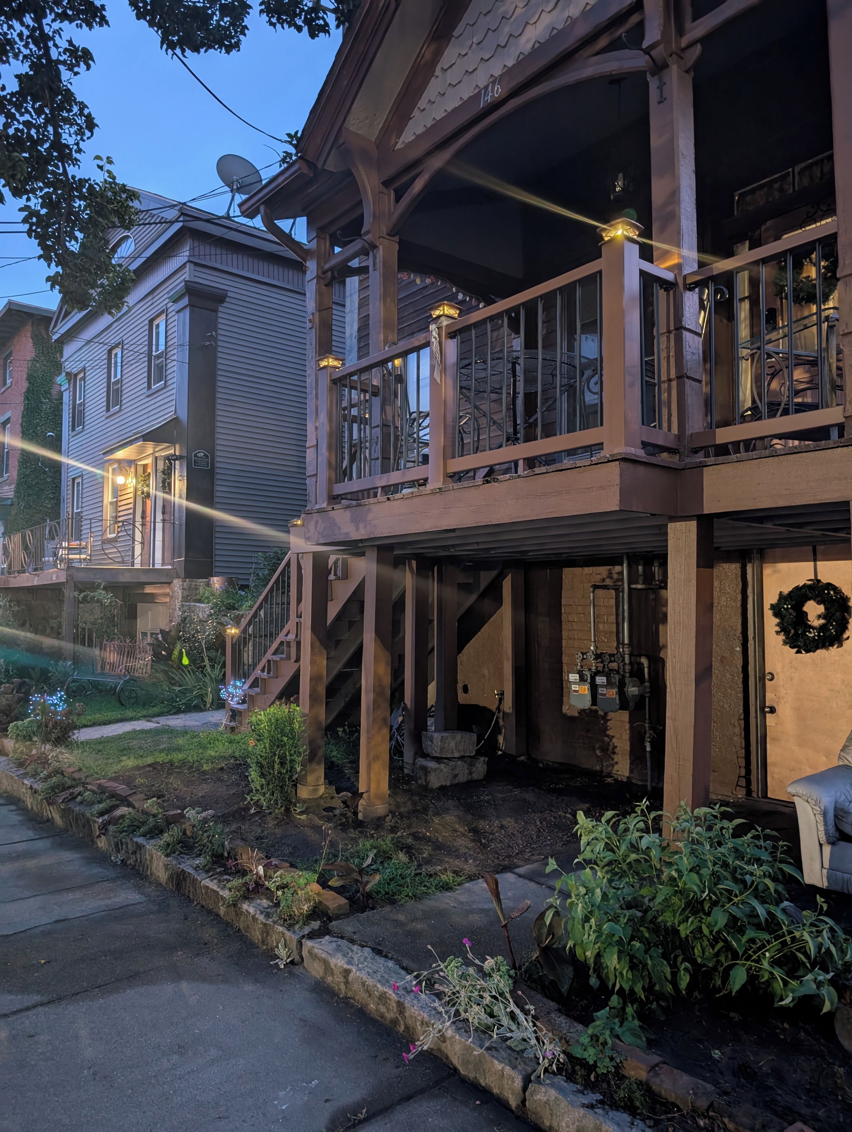 A two-story house with a balcony, a visible garage, and a front yard with plants.