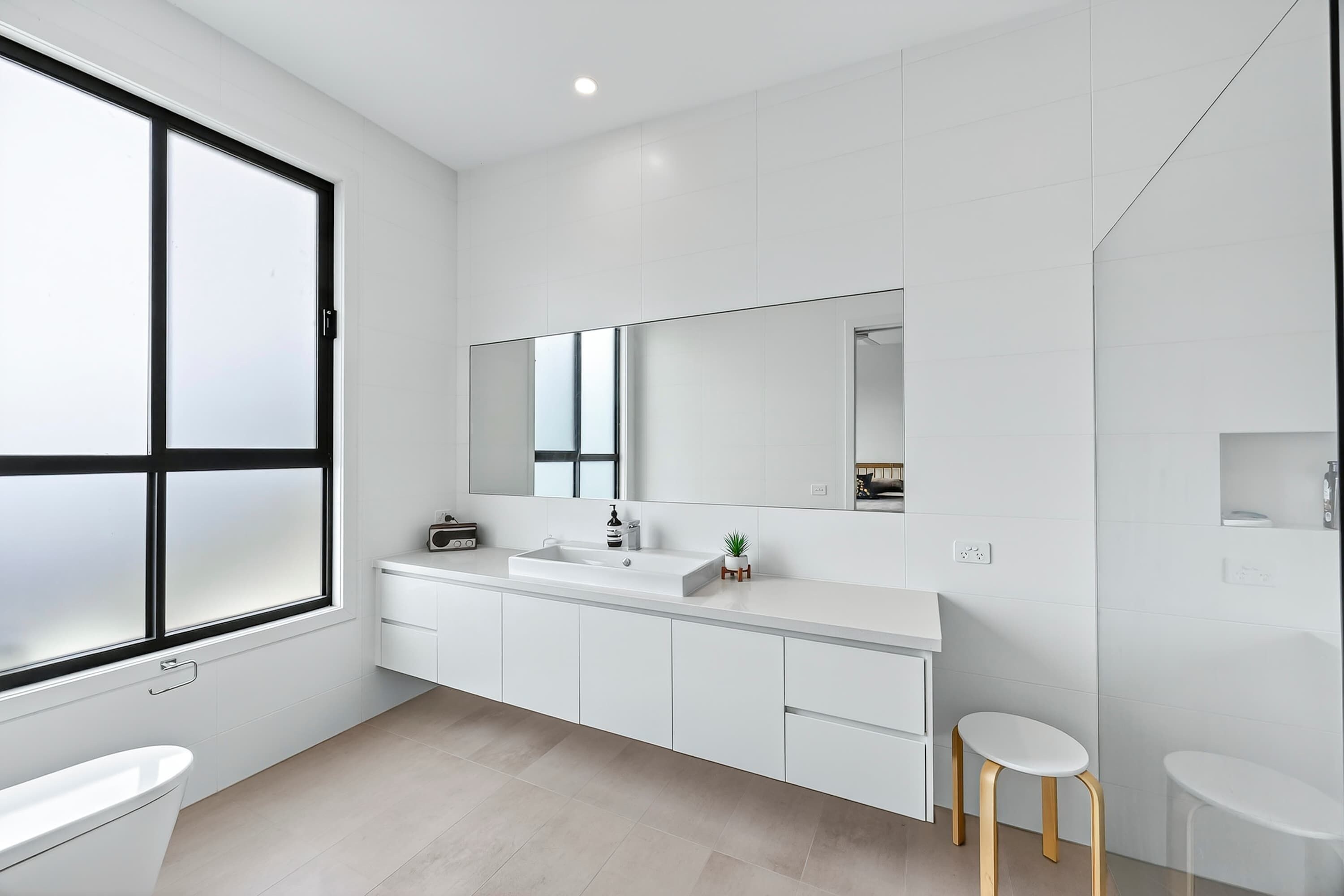 Une salle de bain moderne avec une grande fenêtre, un lavabo, un miroir et deux tabourets.