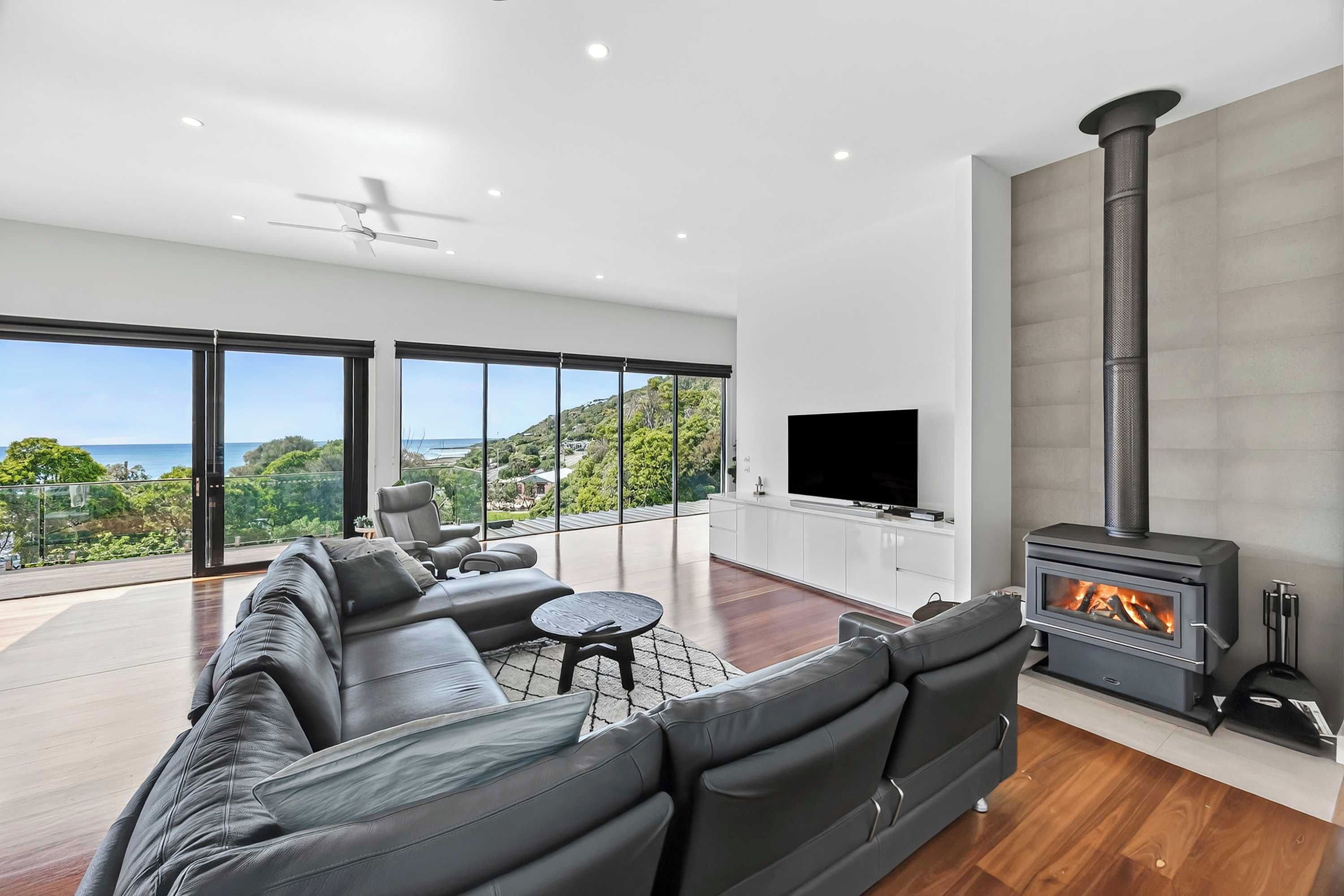 A modern living room with a large black leather sofa, a flat-screen TV, and a wood-burning stove.