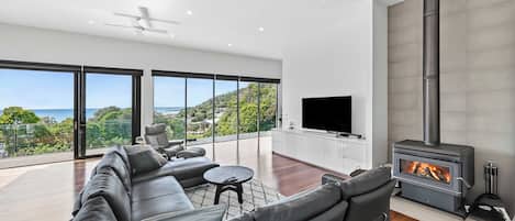 A modern living room with a large black leather sofa, a flat-screen TV, and a wood-burning stove.