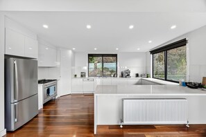 A modern kitchen with white cabinetry, a stainless steel refrigerator, an oven, a dishwasher, and a large window providing a view of the outdoors. - Wye Not  Panorama Ocean Views (Wye River)