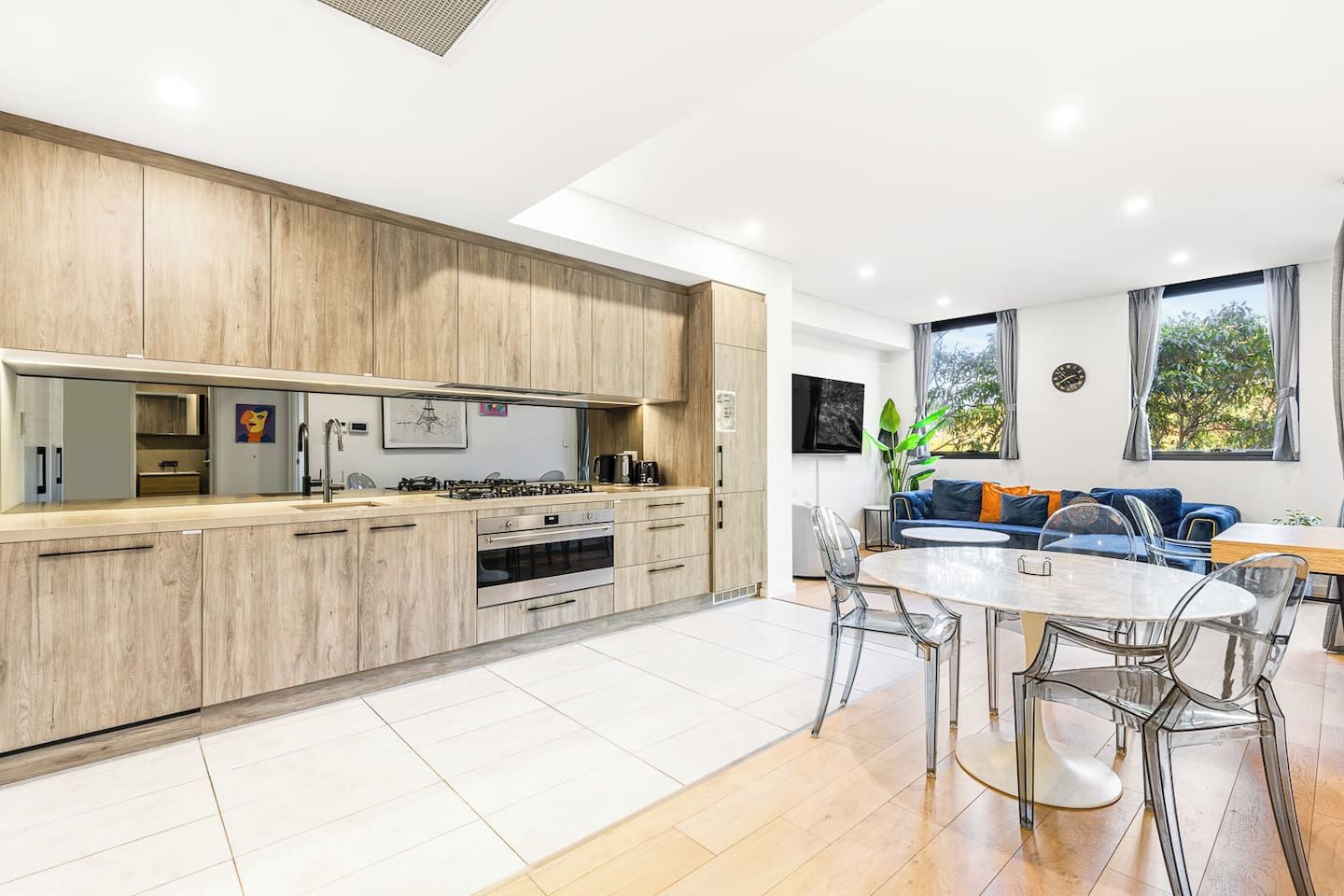 A modern kitchen with wooden cabinets, a built-in oven, and a dining area with a glass table and chairs.