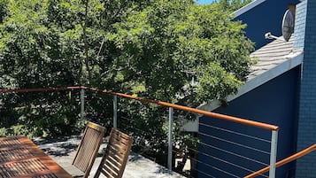 An outdoor seating area with a table and chairs, a metal railing, and a tree providing shade.
