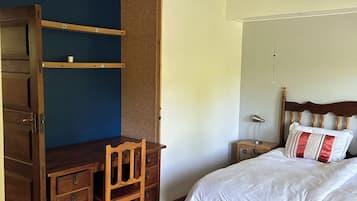A bedroom with a bed, a desk, a chair, a ceiling fan, and a nightstand.