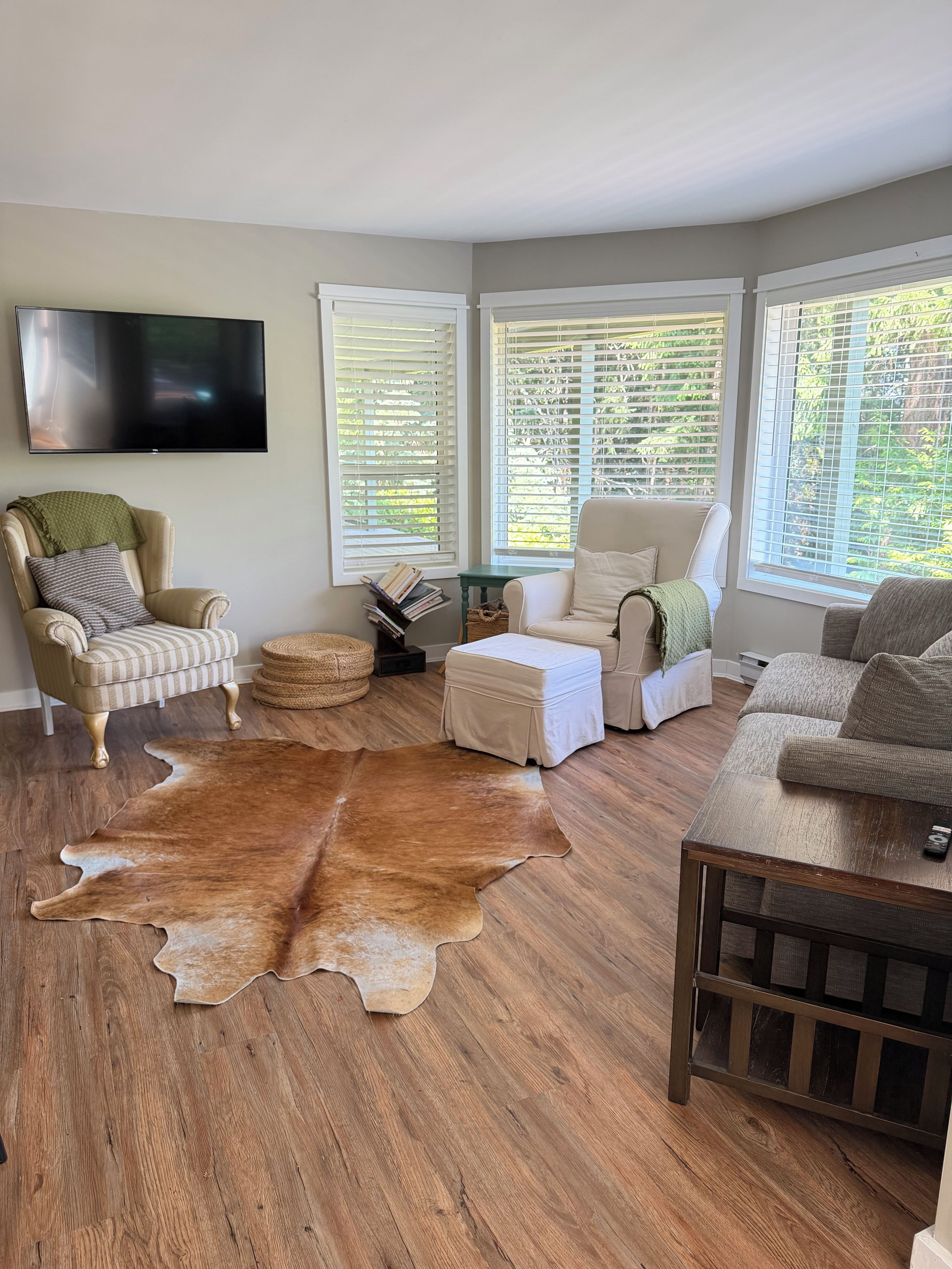 Una sala de estar con un tapete grande de cuero, dos sillones, un sofá, una mesa de centro y un televisor de pantalla plana montado en la pared.