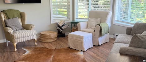 Una sala de estar con un tapete grande de cuero, dos sillones, un sofá, una mesa de centro y un televisor de pantalla plana montado en la pared.