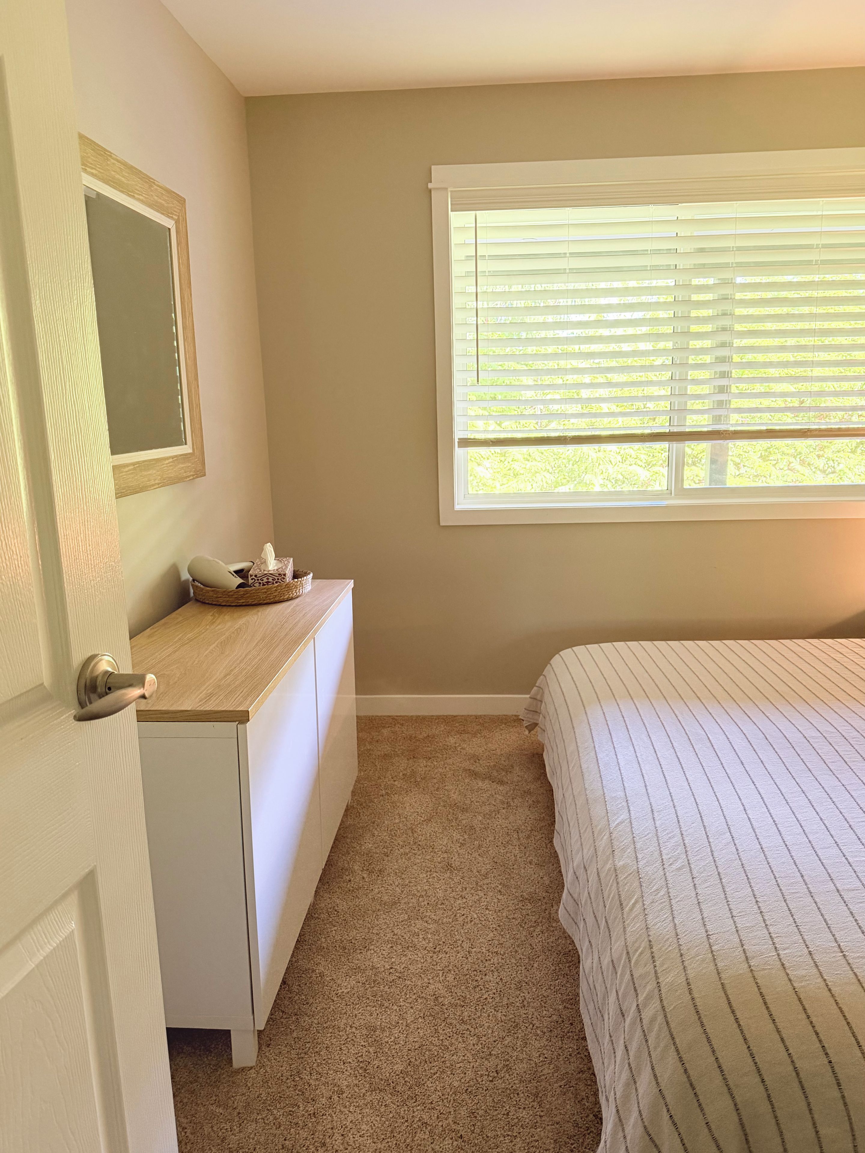 A bedroom with a bed, a dresser, a mirror, and a window with blinds.
