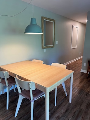 A dining area with a wooden table and chairs, a pendant light, and a mirror on the wall.