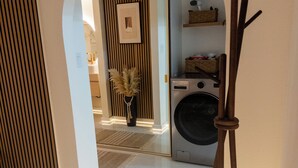 A hallway with a washing machine, a wooden stand, and a framed picture on the wall. - Vrbo Property (Glendale)