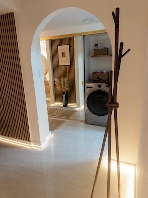 Un couloir avec un lave-linge, un meuble en bois et un tableau encadré accroché au mur.