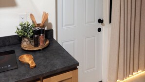 A kitchen with a countertop, wooden cabinets, a white door, and a hanging plant. - Vrbo Property (Glendale)