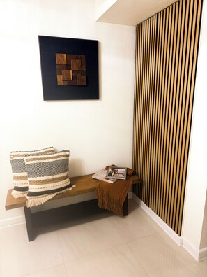 Ein Zimmer mit einer Holzbank, einem gerahmten abstrakten Kunstwerk, einer gemusterten Decke und einer Zeitschrift auf der Bank.