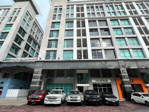 A multi-story building with a row of parked cars in front. - Capital O 90985 Margo Hotel KK (Kota Kinabalu)