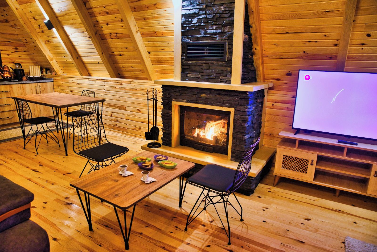 A cozy wooden interior with a fireplace, a dining table, chairs, and a television.