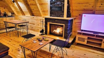 A cozy wooden interior with a fireplace, a dining table, chairs, and a television.