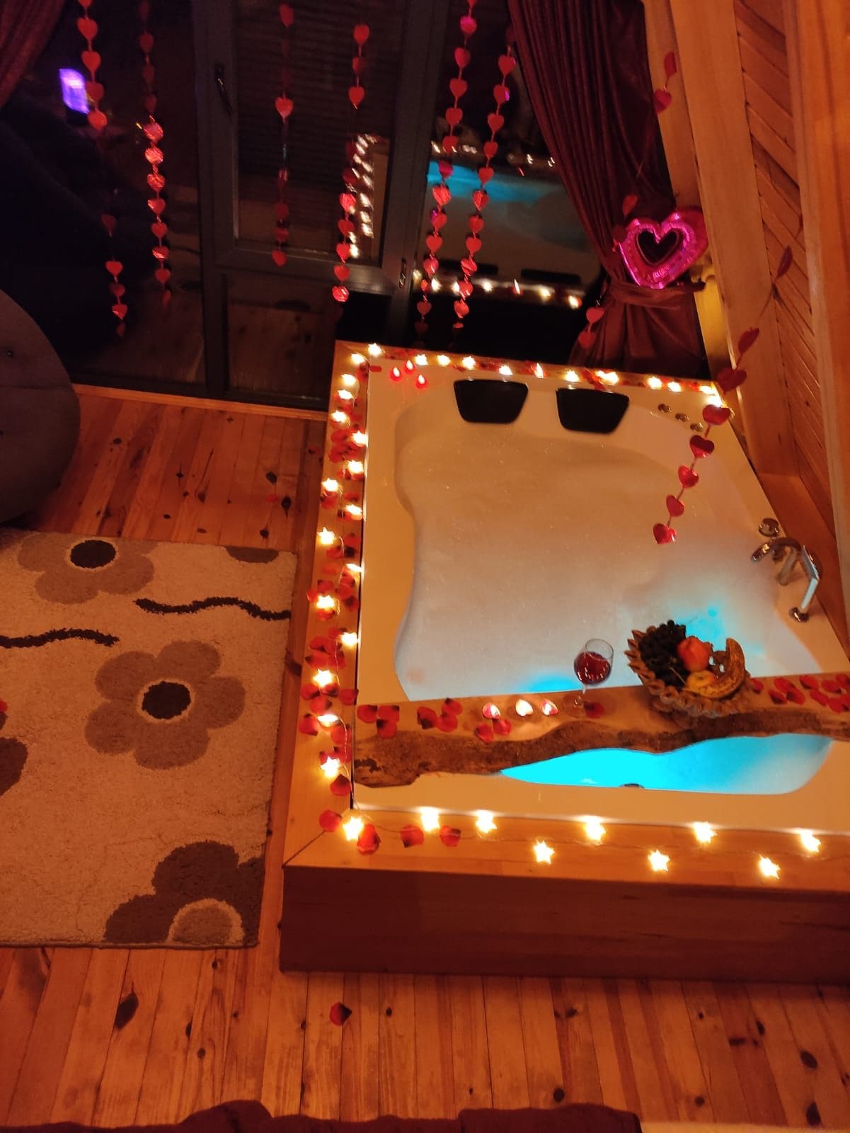 Una habitación con una bañera grande, suelo de madera y una alfombra con estampado floral.