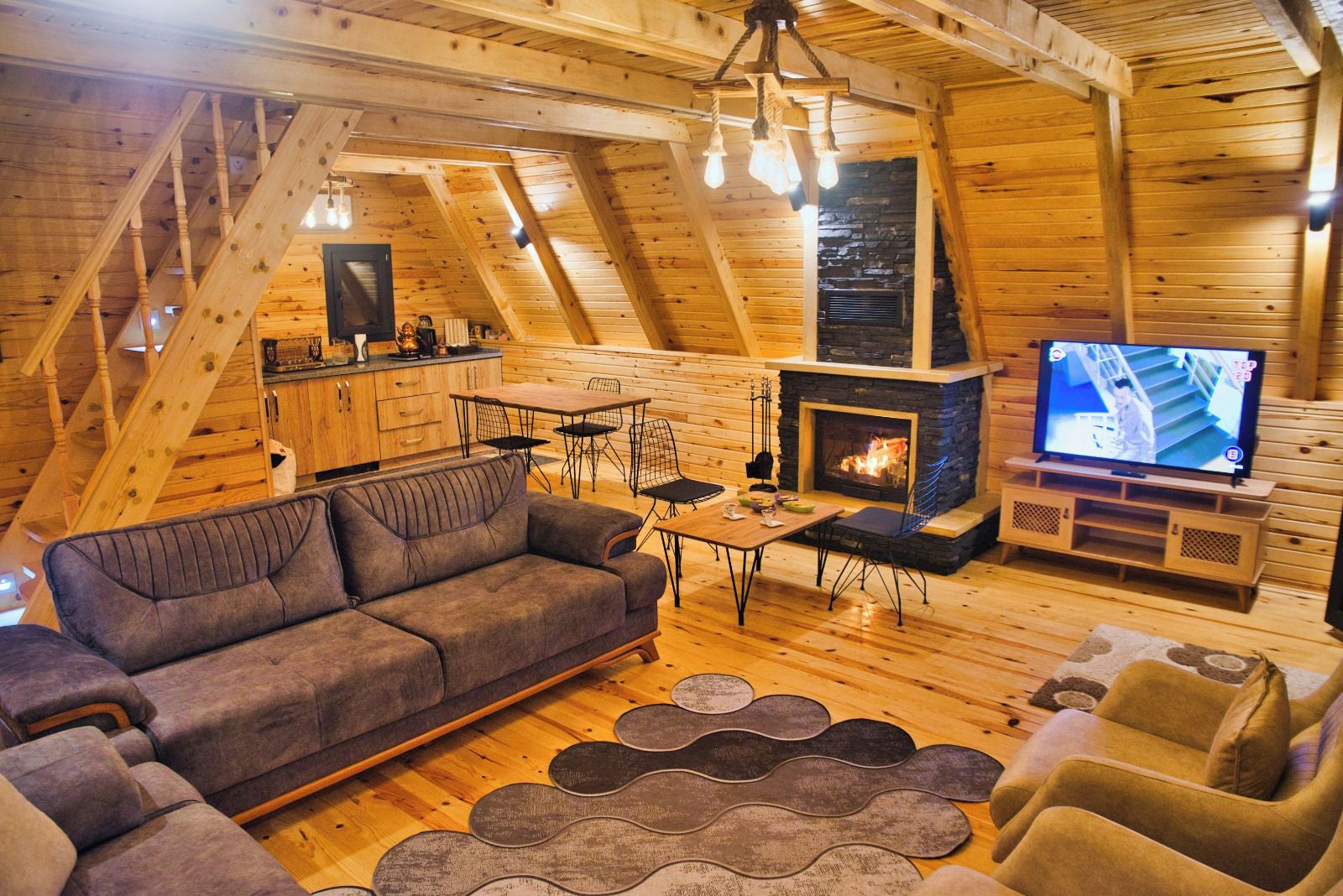 Un acogedor loft con techo de madera, un sofá, una mesa de comedor, sillas, chimenea y televisor.