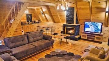 Un acogedor loft con techo de madera, un sofá, una mesa de comedor, sillas, chimenea y televisor.