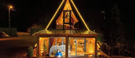 A triangular wooden structure with a glass door, a chair, and a table inside.