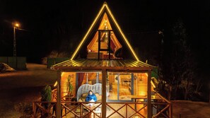 Una estructura de madera triangular con puerta de cristal, una silla y una mesa en su interior.