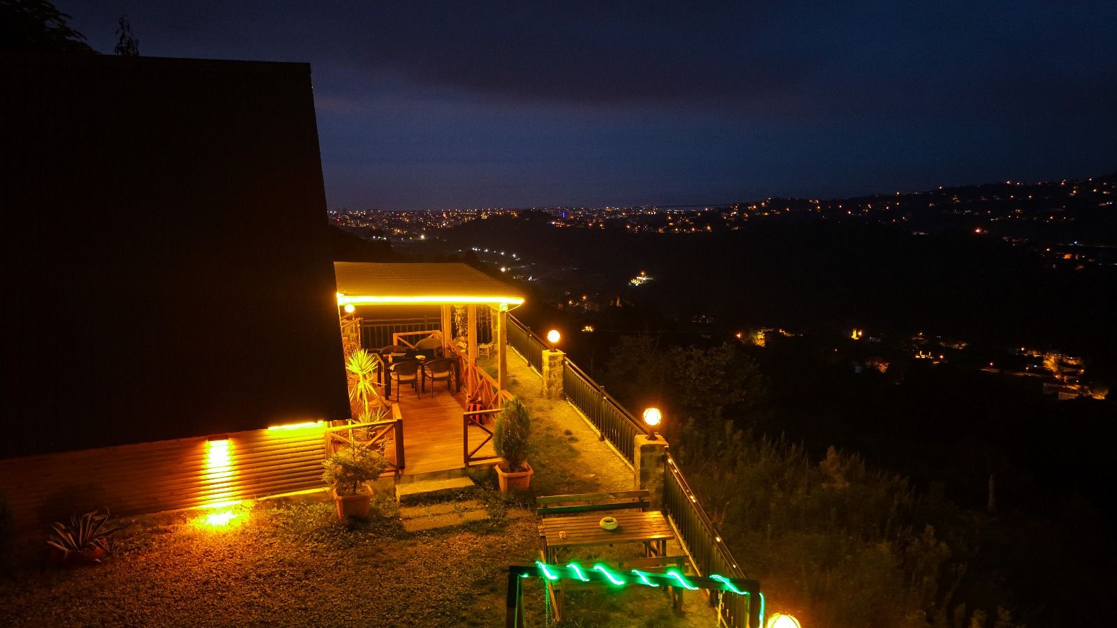 A nighttime view of a house with a lit porch and a view of a cityscape.