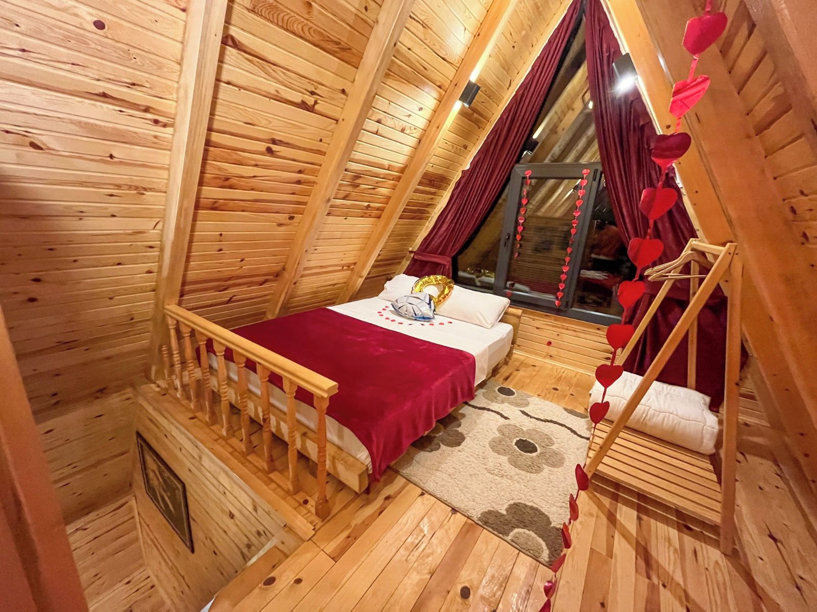 A cozy wooden room with a bed, a window with curtains, and a wooden chair.