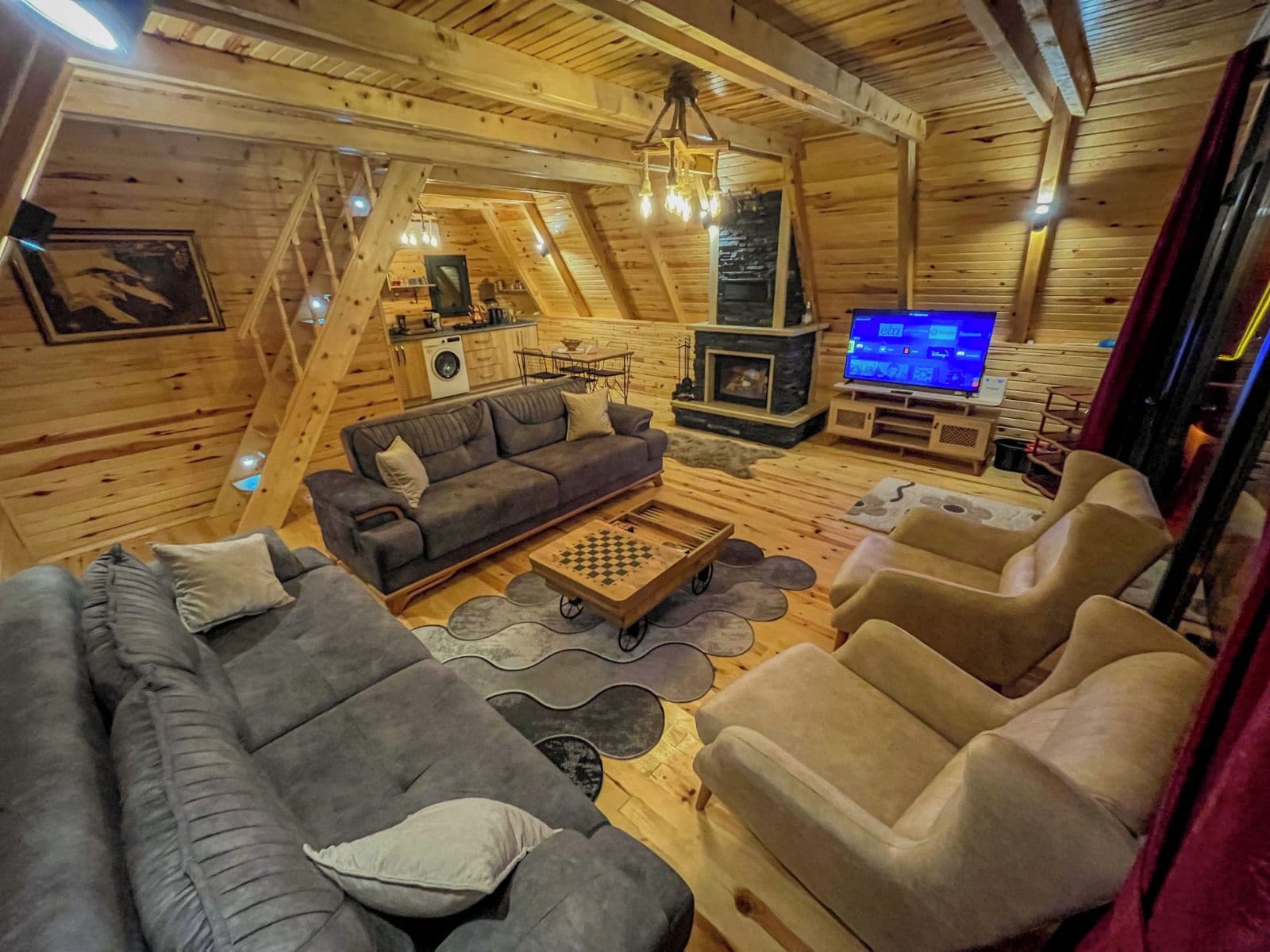 A cozy log cabin interior with a sofa, armchairs, a fireplace, and a television.