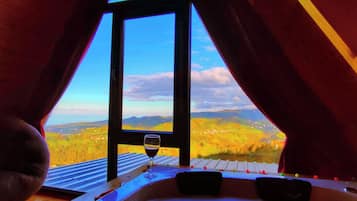 Vista interna de um quarto com uma grande janela, uma banheira de hidromassagem e um copo de vinho tinto.