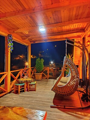 A wooden deck with a hanging chair, a table, and a potted plant.
