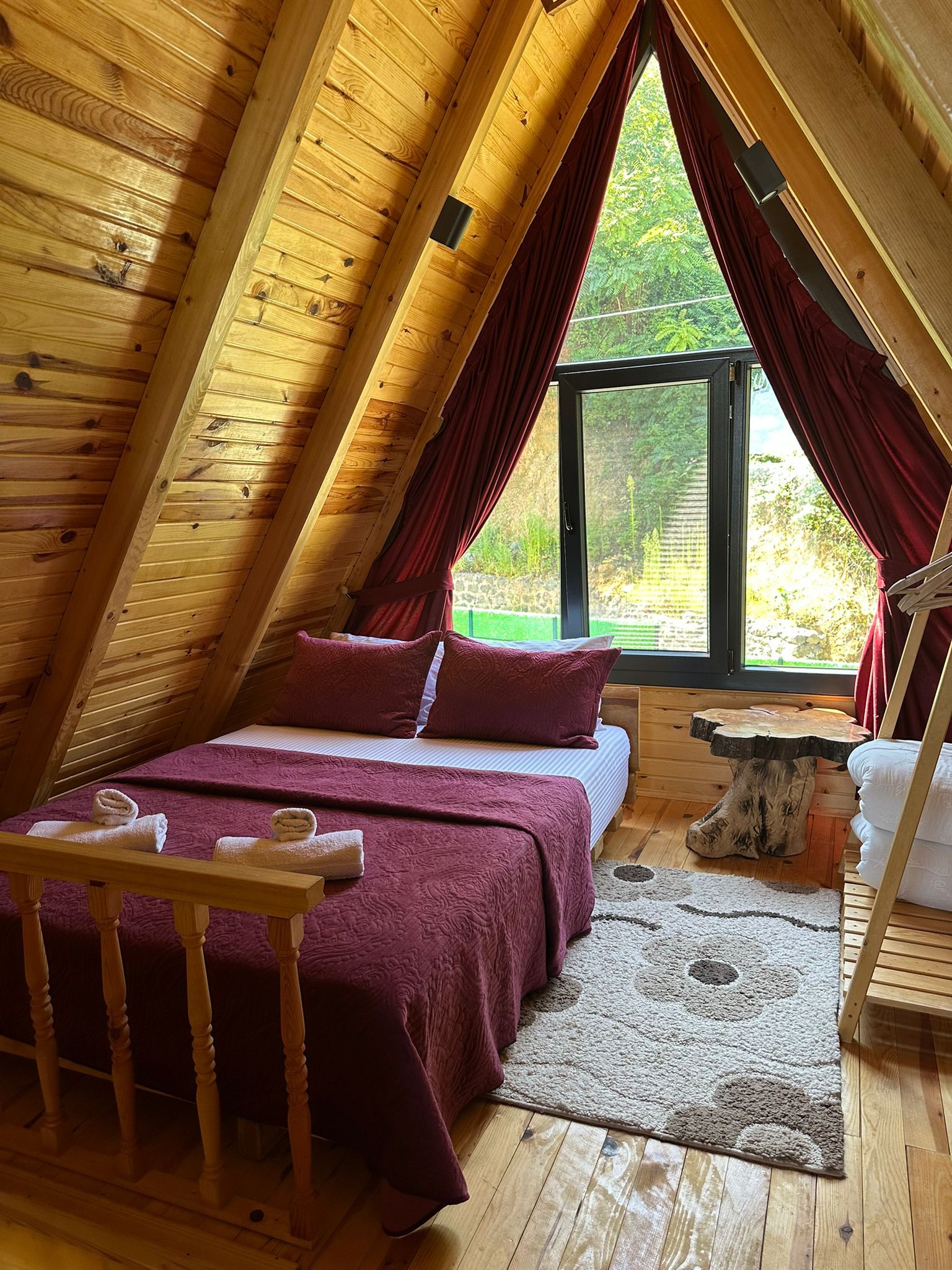 A cozy attic bedroom with a bed, a wooden table, and a window with curtains.