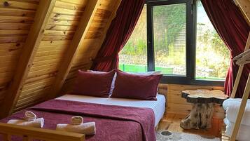 A cozy attic bedroom with a bed, a wooden table, and a window with curtains.