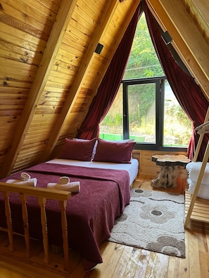 A cozy attic bedroom with a bed, a wooden table, and a window with curtains. - Dere bungalov (Ardeşen)