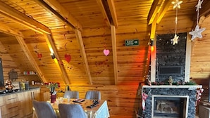 En hyggelig indretning med træloft, spiseplads med bord og stole, pejs og skilt, der viser en udgang.