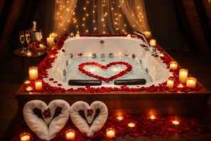 A romantic setting with a bathtub surrounded by candles and rose petals, two heart-shaped towels, and a bottle of champagne. - Dere bungalov (Ardeşen)