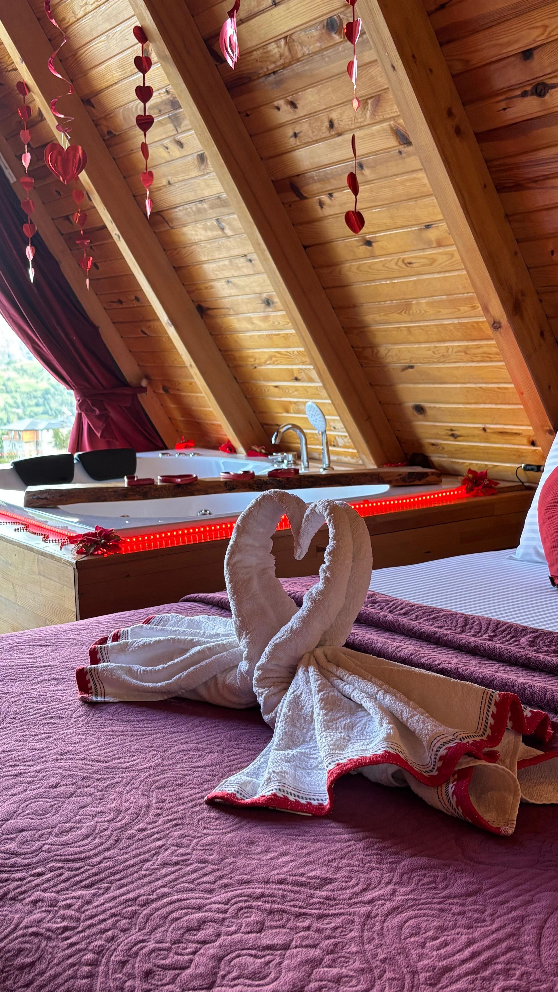 A bedroom with a wooden ceiling, a bed with a red heart-shaped decoration, and a towel shaped like a swan.