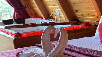 A bedroom with a wooden ceiling, a bed with a red heart-shaped decoration, and a towel shaped like a swan.