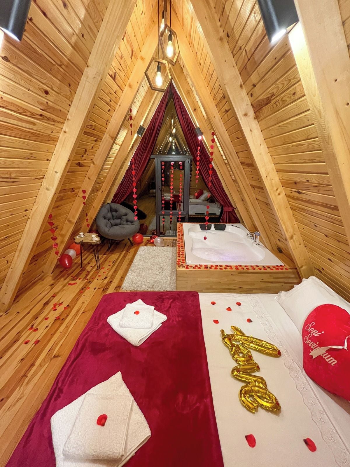 A cozy attic bedroom with a sloped ceiling, a bed with a red and white bedspread, and a small seating area with a gray bean bag.