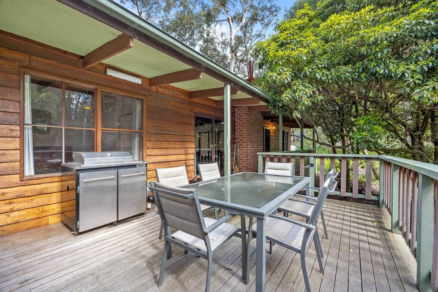 Une terrasse en bois avec une table et des chaises en verre, un barbecue et une cheminée en briques.