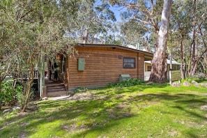 A wooden cabin with a porch, surrounded by trees and grass. - Tanglewood Cottage | Halls Gap Accommodation (Halls Gap)