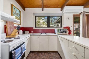 A compact kitchen with a stove, sink, and a window providing natural light. - Tanglewood Cottage | Halls Gap Accommodation (Halls Gap)