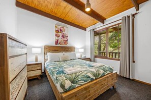 A bedroom with a wooden bed, two bedside tables, a nightstand, a window with curtains, and a ceiling light. - Tanglewood Cottage | Halls Gap Accommodation (Halls Gap)