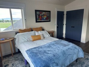 Un dormitorio con cama, mesita de noche, ventana, puerta y un cuadro en la pared.