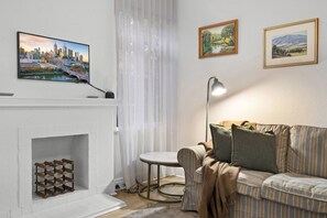A living room with a fireplace, a television mounted above it, a sofa, and two framed landscape paintings on the wall. - Poolside Art Deco Apartment in St Kilda West (Saint Kilda West)
