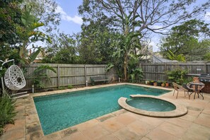 Ein Garten mit Swimmingpool und Whirlpool, umgeben von einem Holzzaun und üppiger Bepflanzung.